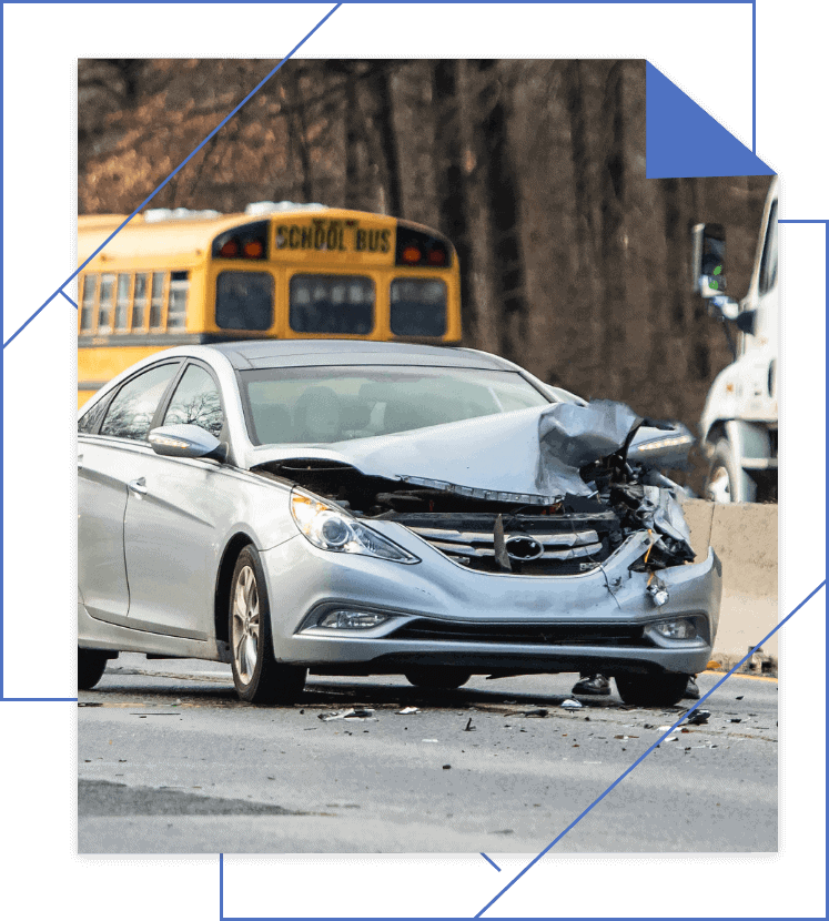 Silver car with front-end damage on a road, school bus and truck in the background.